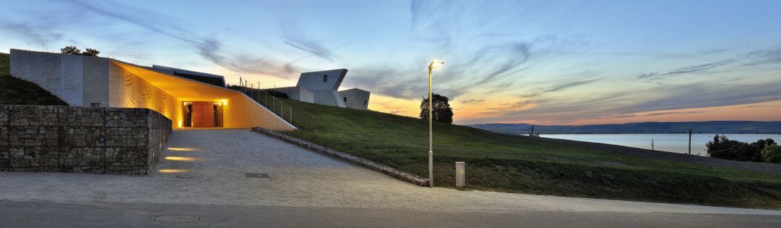 nocne ujęcie wejścia do budynku, które prowadzi z zewnątrz wprost do holu wkomponowanego w teren; w tle po prawej stronie widać Zbiornik Věstonice