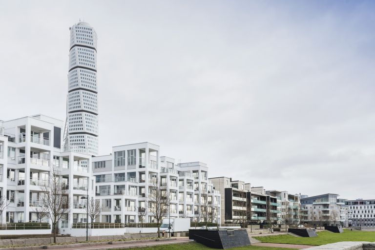 Modern residential and commercial buildings along the waterfront in Malmö's Western Harbour, with the Turning Torso visible in the distance.