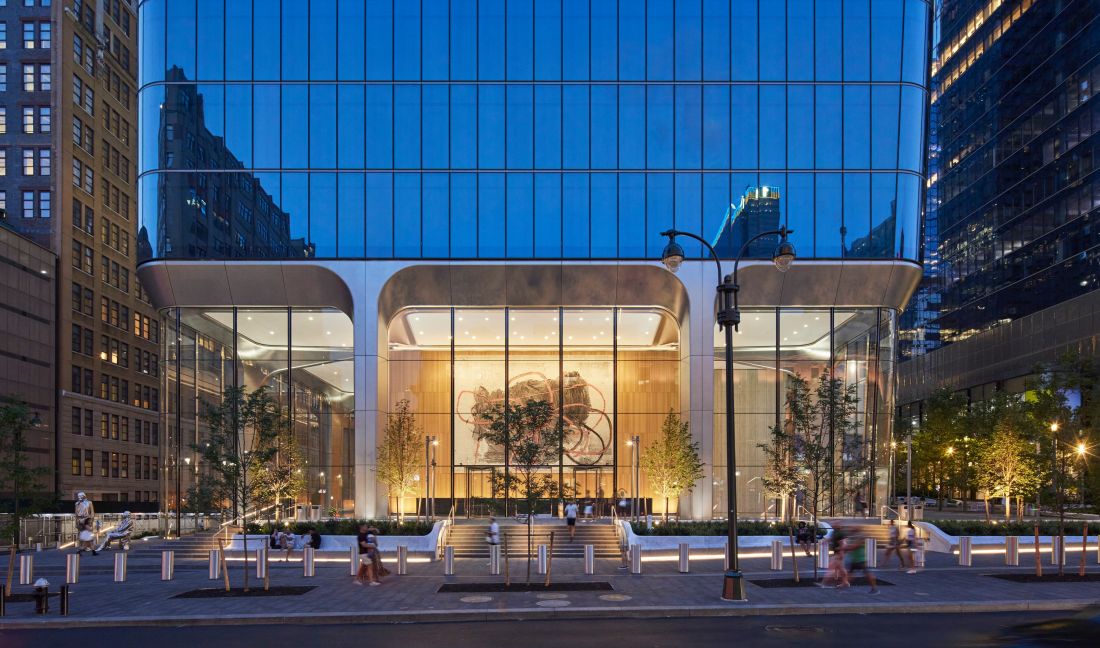 Manhattan West o zmierzchu z dużym przeszklonym wejściem, abstrakcyjną sztuką wewnątrz i małymi drzewami z przodu