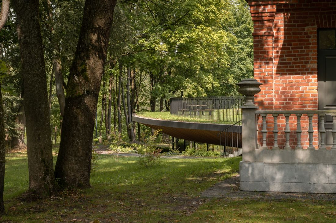 Historyczny dwór w Poniewieżu - widok na historyczny budynek z czerwonej cegły i nową konstrukcję schowaną pod ziemią 