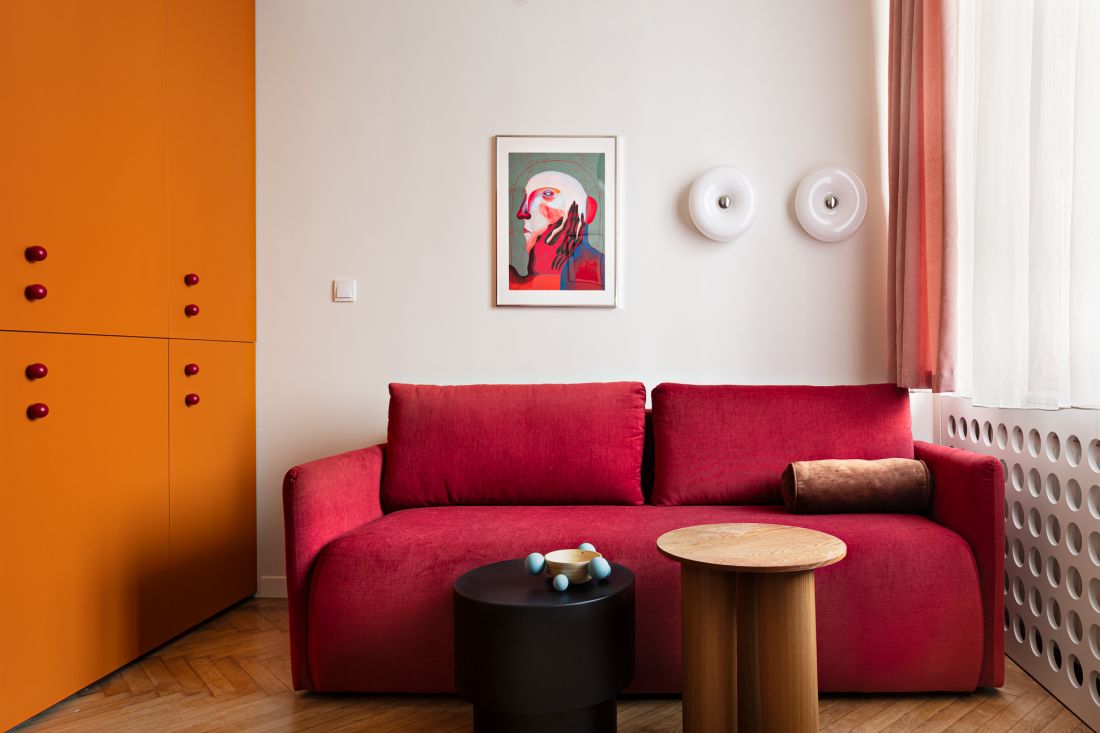Czerwona rozkładana sofa doskonale współgra z pomarańczową szafą