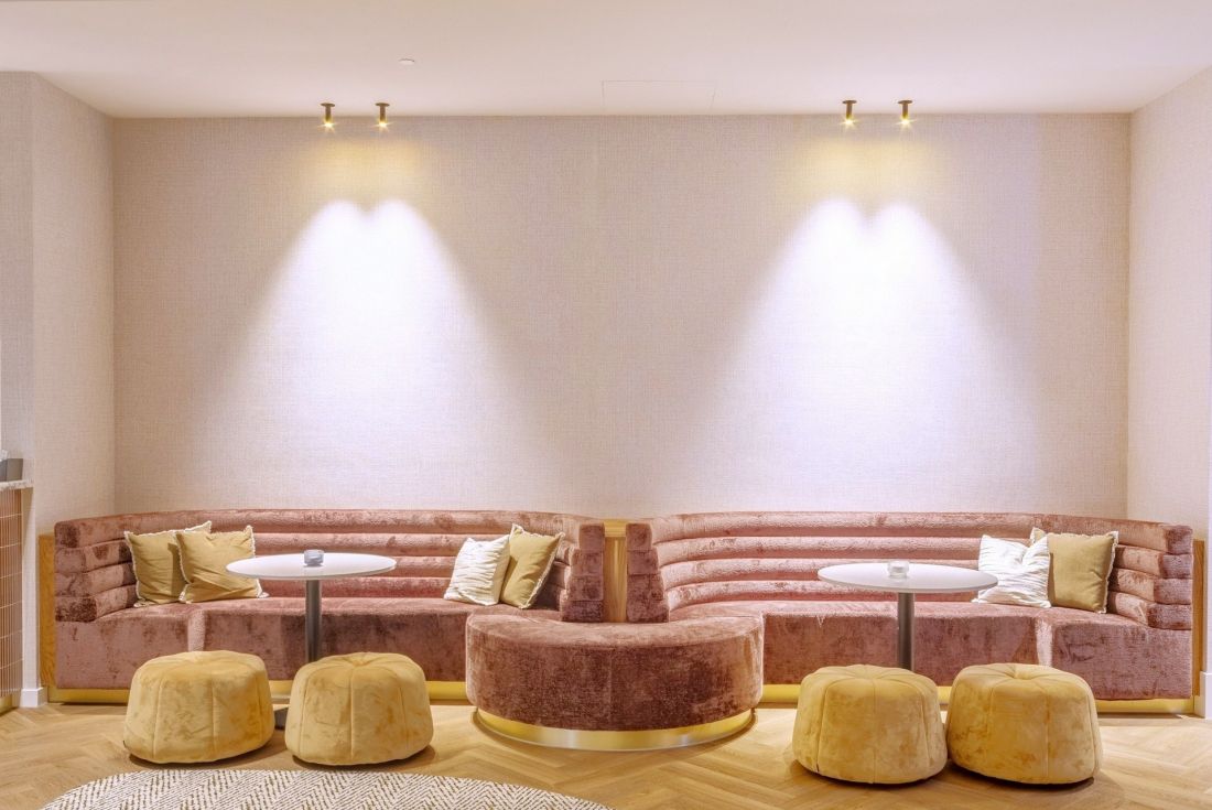 Falujące kształty akustycznych sufitów Eleganza marki Knauf Ceiling Solutions współgrają z kształtami recepcji, a pluszowe, miękkie sofy w złotej i różowej kolorystyce wzmacniają efekt przyjaznej akustyki i wypoczynku 