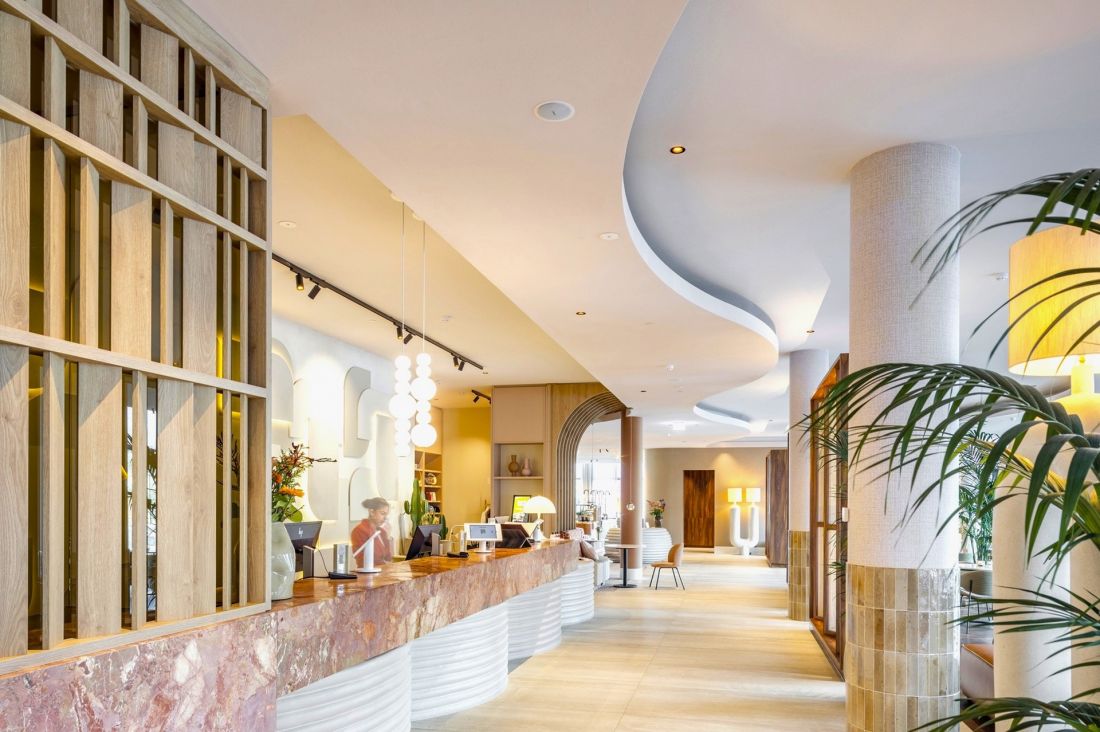 Falujące kształty akustycznych sufitów Eleganza marki Knauf Ceiling Solutions współgrają z kształtami recepcji, a pluszowe, miękkie sofy w złotej i różowej kolorystyce wzmacniają efekt przyjaznej akustyki i wypoczynku 