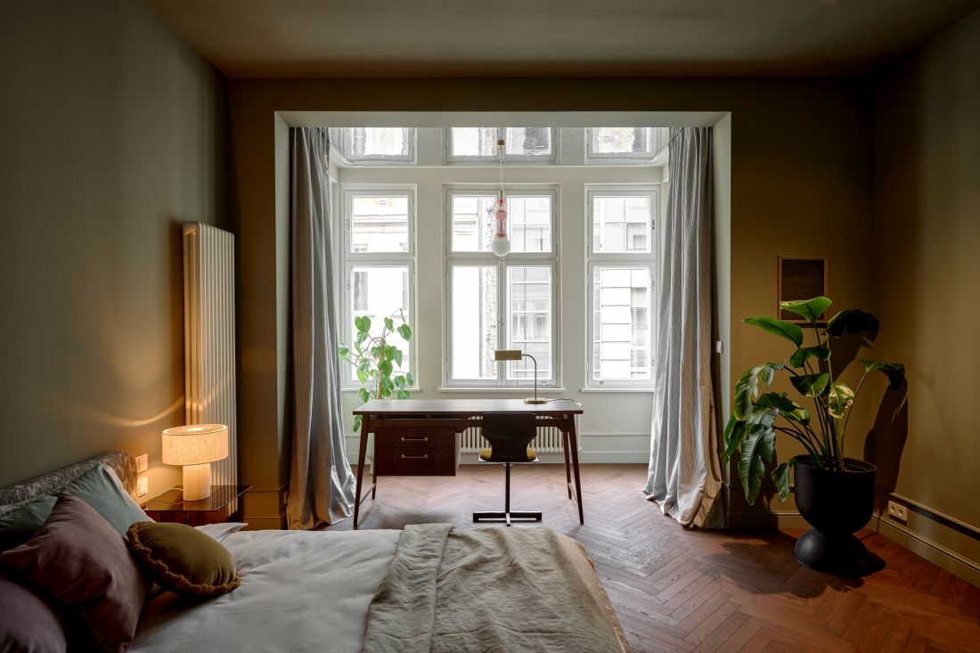 W sypialni najważniejsze są światło i miękkość. Łóżko ustawiono przy przygaszonej zielonej ścianie, a wykusz zamieniono w spokojny kąt do pracy z widokiem na centrum Wrocławia