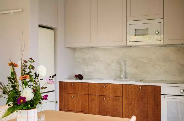 Fornirowane, frezowane fronty dolnych szafek kuchennych w karmelowym kolorze, architektka zestawiła z prostymi, beżowymi frontami szafek górnych