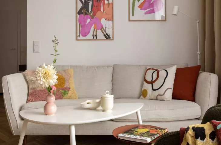 w salonie nad kremową kanapą umieszczono kolorowe ilustracje autorstwa Karoliny Pawelczyk