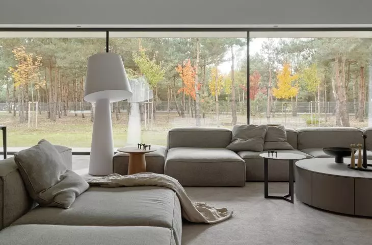 Large glass windows give a soothing view of the trees on the plot and in the immediate vicinity; one of the segments of the modular sofa faces the window, in opposition to the TV set