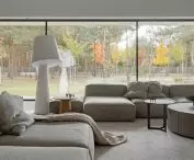 Large glass windows give a soothing view of the trees on the plot and in the immediate vicinity; one of the segments of the modular sofa faces the window, in opposition to the TV set