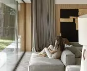 Large glass windows give a soothing view of the trees on the plot and in the immediate vicinity; one of the segments of the modular sofa faces the window, in opposition to the TV set