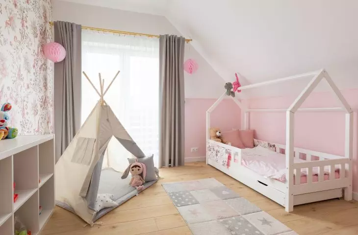 The children's bed is shaped like a house with a gabled roof