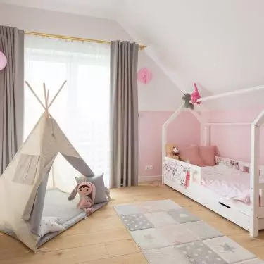 The children's bed is shaped like a house with a gabled roof