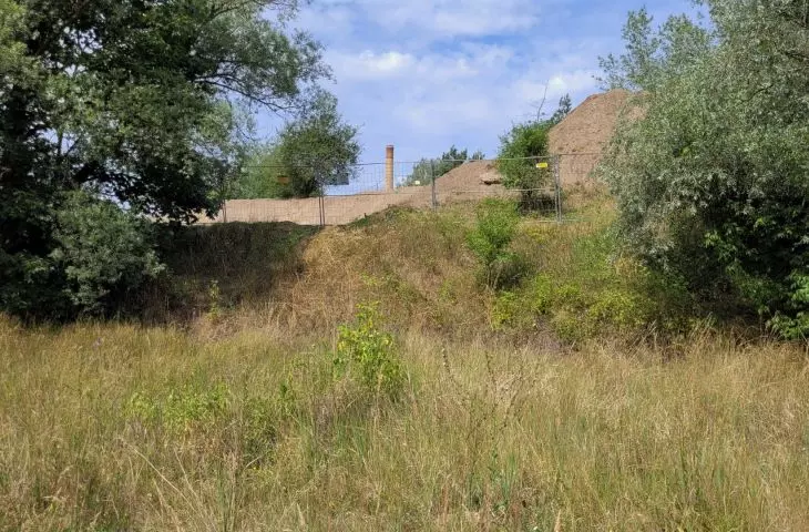 Southern tip of Ostrów Tumski, left bank of the relief canal; excavations visible, behind them the chimney of the Old Gasworks