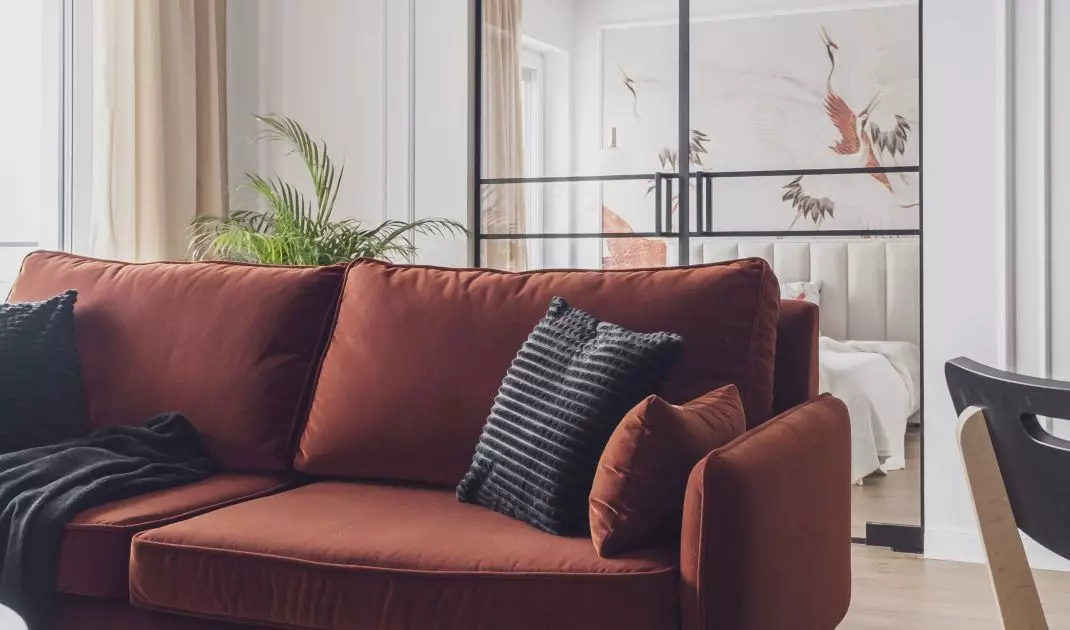 Ceglasta sofa ożywia stonowaną przestrzeń