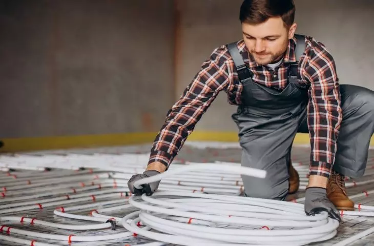 A professional installs a water floor heating system. This solution can work with heat pumps and other types of heating. 
