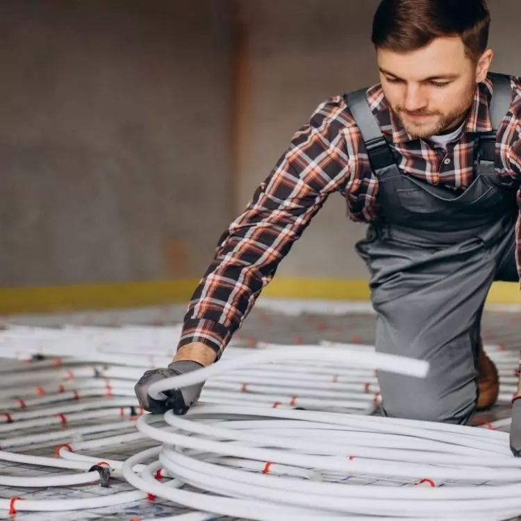 Fachowiec układa system wodnego ogrzewania podłogowego. Rozwiązanie to może współpracować z pompami ciepła i innymi typami ogrzewania. 
