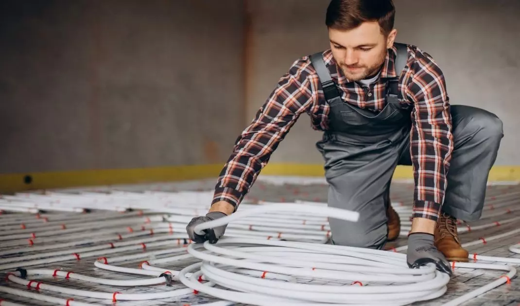 A professional installs a water floor heating system. This solution can work with heat pumps and other types of heating. 
