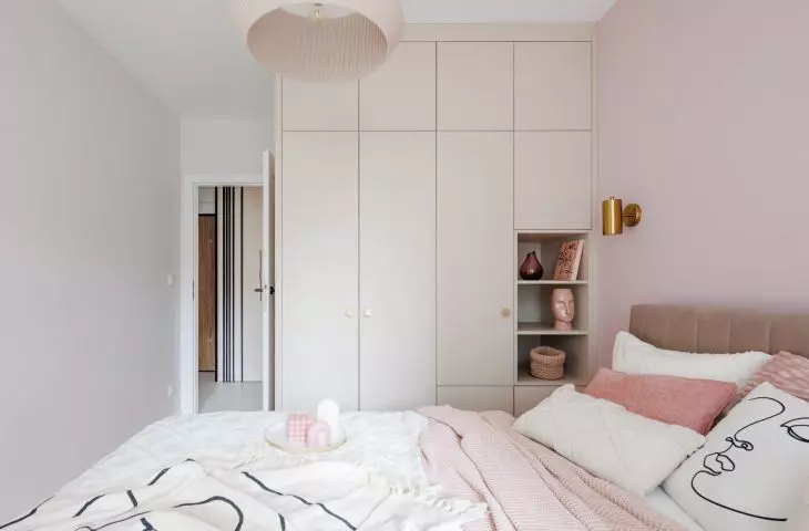 A pink lamp with a crinkle shade hangs over the bed
