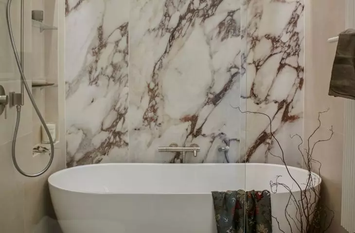 The wall behind the bathtub has been decorated with large-format tiles with a marble pattern