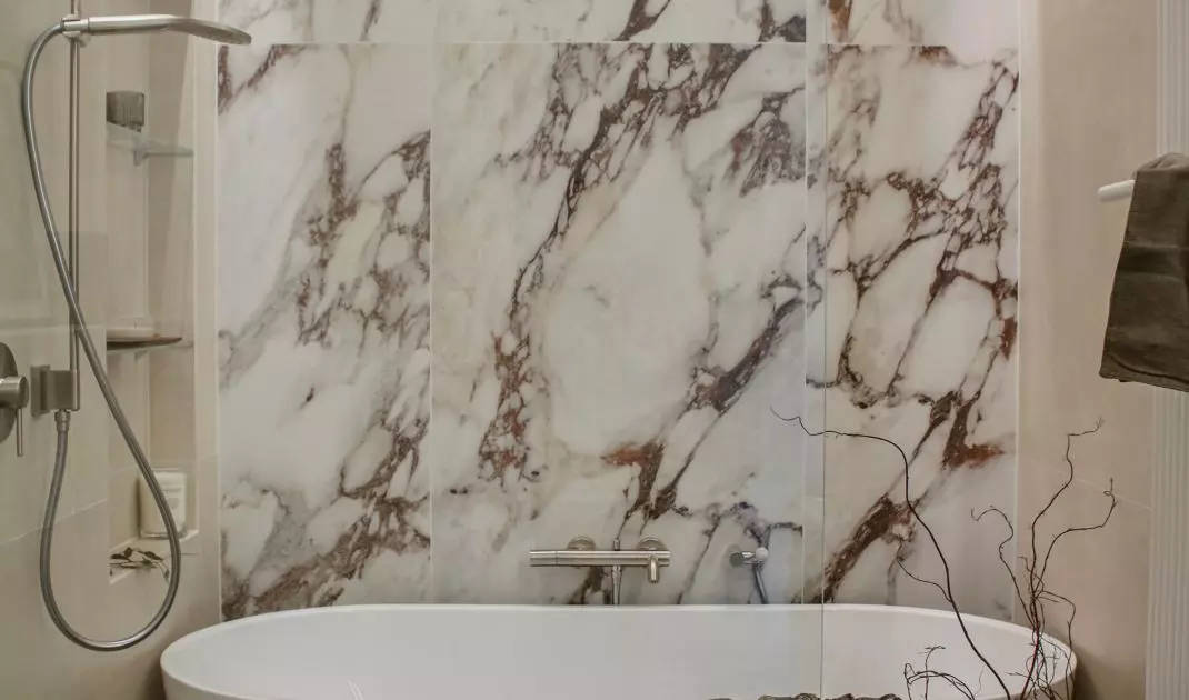 The wall behind the bathtub has been decorated with large-format tiles with a marble pattern