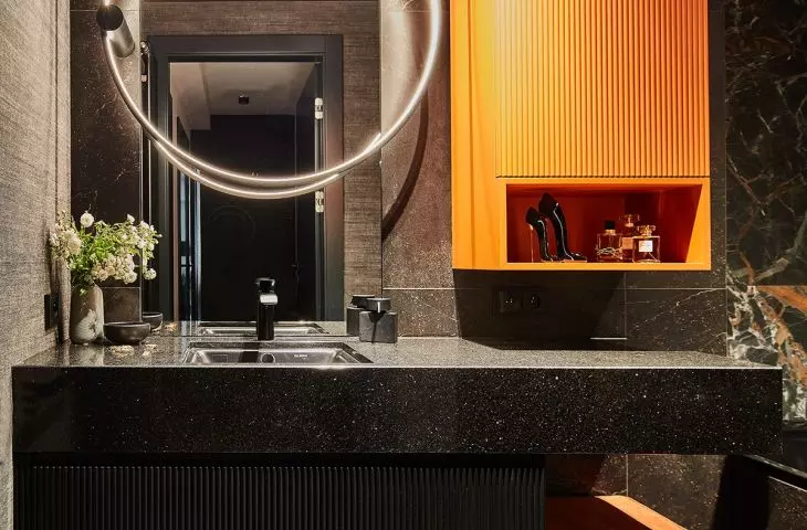 The colorful accents of the bathroom are the orange cabinet and pouffe