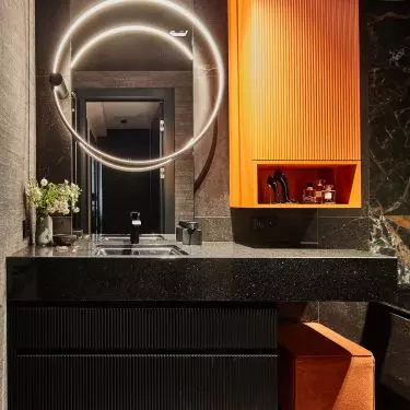 The colorful accents of the bathroom are the orange cabinet and pouffe