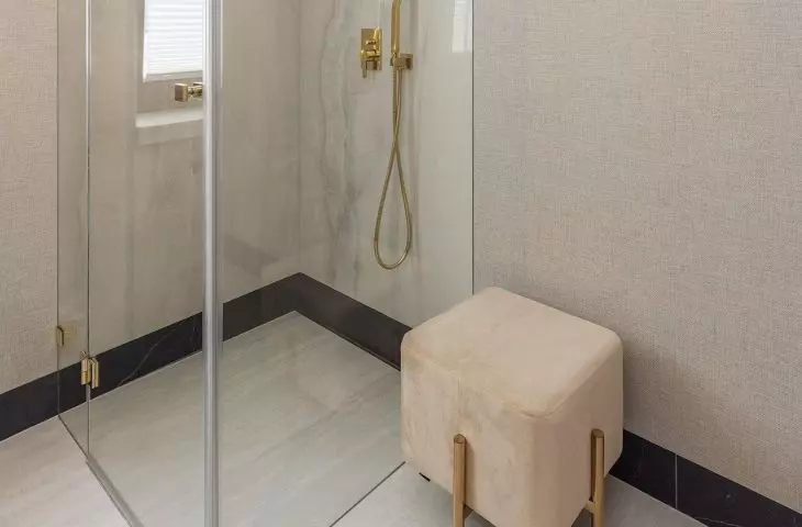 A pouf with golden legs stood near the shower stall