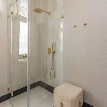 A pouf with golden legs stood near the shower stall