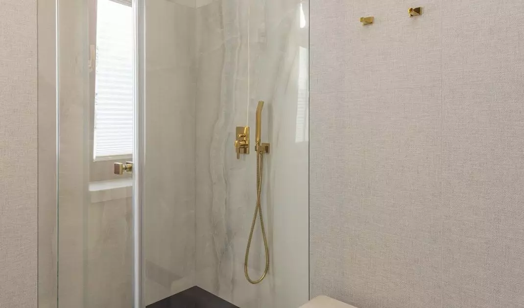 A pouf with golden legs stood near the shower stall