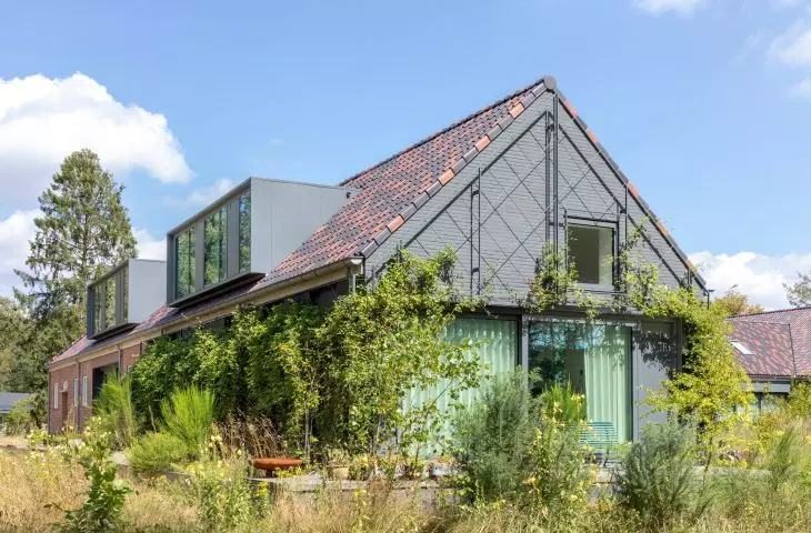 A restored red brick building with modern celadon accents and an ivy-covered wall, surrounded by wild grass and flowers