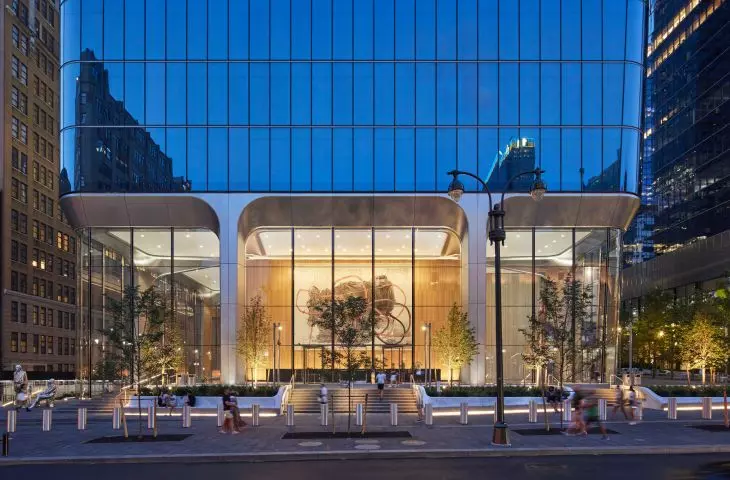 Manhattan West o zmierzchu z dużym przeszklonym wejściem, abstrakcyjną sztuką wewnątrz i małymi drzewami z przodu