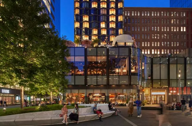 Miejski plac przy Manhattan West o zmierzchu, w tle nowoczesne budynki o szklanych ścianach i ludzie siedzący na zakrzywionej, designerskiej ławce