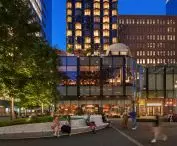 Miejski plac przy Manhattan West o zmierzchu, w tle nowoczesne budynki o szklanych ścianach i ludzie siedzący na zakrzywionej, designerskiej ławce