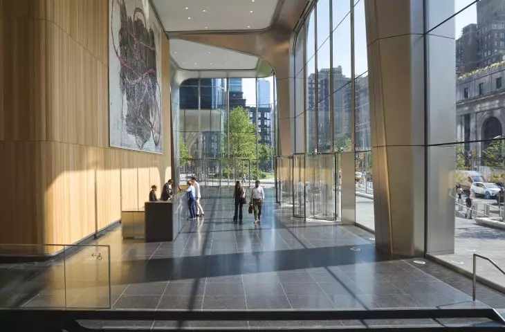 A lobby in a high-rise building with large windows, a wooden wall with an abstract painting, a dark stone floor and a revolving glass door