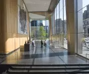 A lobby in a high-rise building with large windows, a wooden wall with an abstract painting, a dark stone floor and a revolving glass door