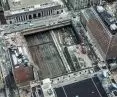 An aerial view of an urban construction site next to the railroad tracks, surrounded by buildings, streets and cars