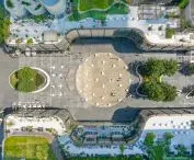 Aerial view of modern city square surrounded by curved buildings with rooftop seating areas and green spaces