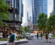 Urban space with trees, outdoor seating areas and people walking around, modern skyscrapers in the background