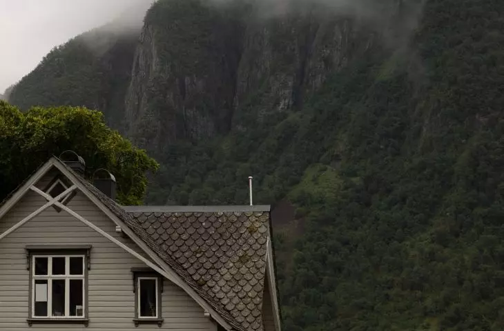 Grey house with a gabled roof and windows against a background of green mountains covered with mist