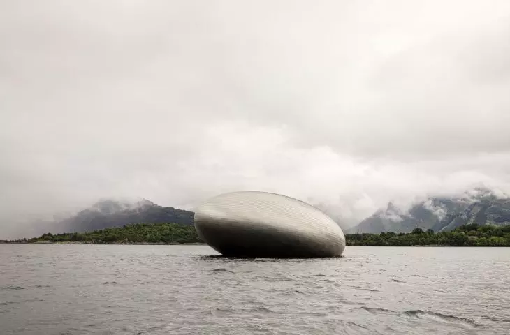 Oval metal structure floating on water with a wooded and mountainous background