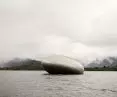 Oval metal structure floating on water with a wooded and mountainous background