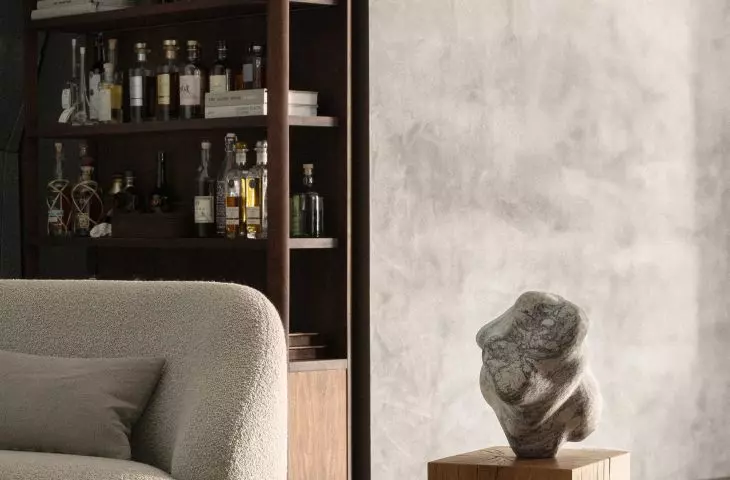 Modern living room with beige armchair, abstract sculpture on wooden pedestal and wooden wine rack