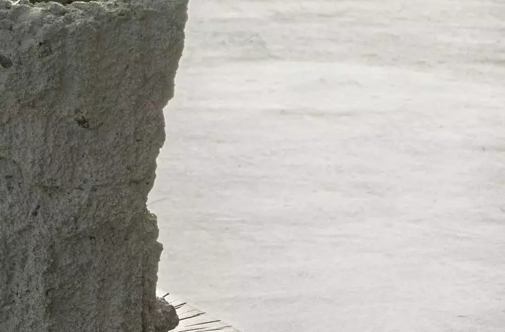 Close-up of a rough gray stone sculpture on a wooden pedestal, with calm water in the background