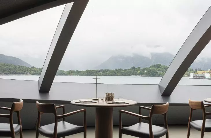 Modern dining room with large slanted windows overlooking the lake and misty hills