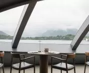 Modern dining room with large slanted windows overlooking the lake and misty hills