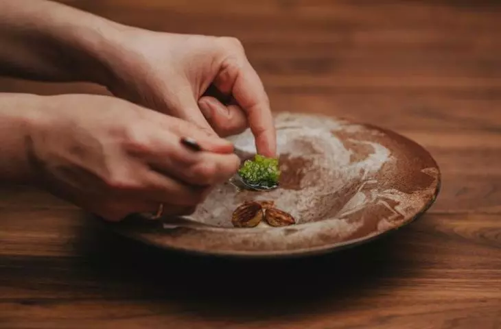 Ręce nakładające łyżką zielone, wykwintne jedzenie na brązowy ceramiczny talerz