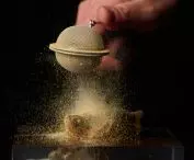 Hand holding a tea brewer releasing fine powder onto an exquisite dish