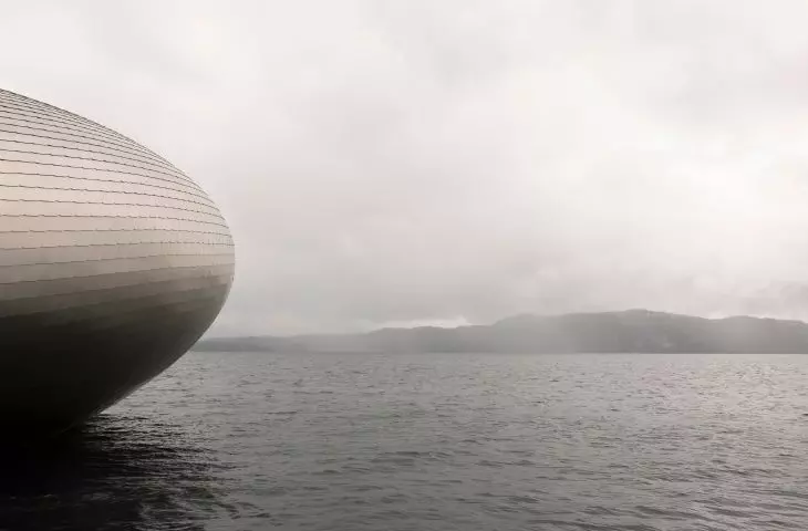 Partial view of a metal building on the water with misty hills in the distance