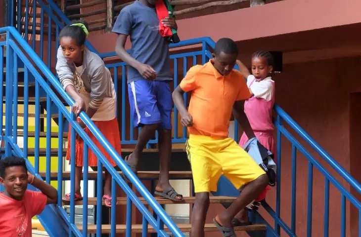 A group of five people descending a staircase with blue railings, against a background of rustic wooden railings