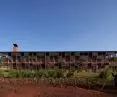 The back of the wooden building of Busajo Campus, in the foreground a gardener watering the green grass