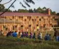 Children sitting on the grass with the large wooden Busajo Campus building in the background